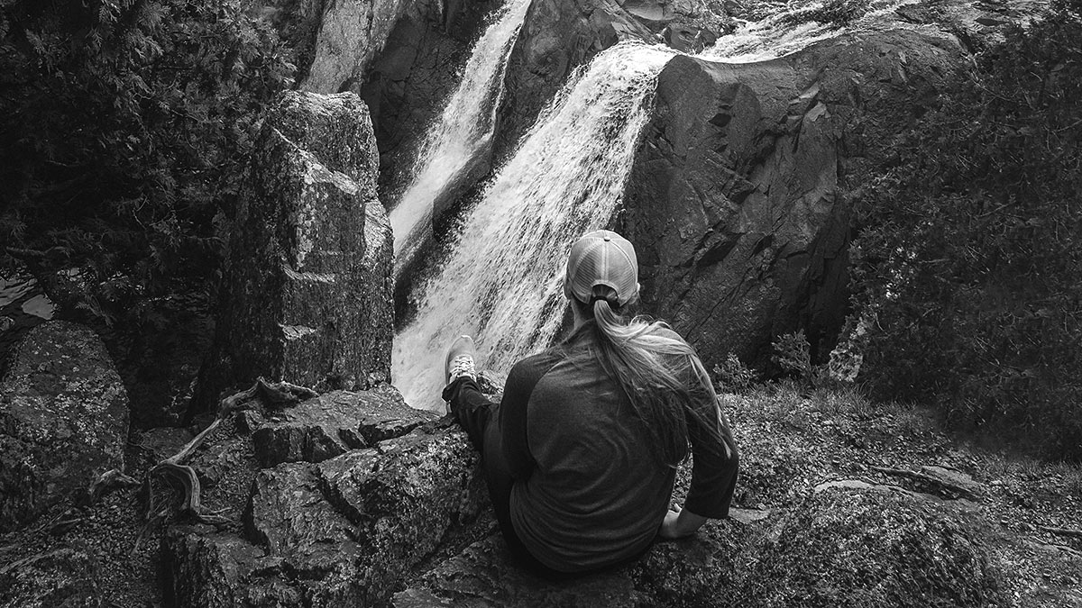 woman seated at rock overlooking waterfall